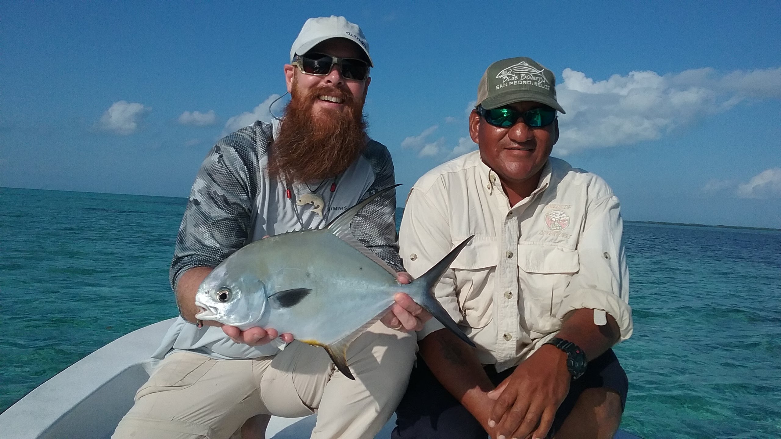 Angler holding a permit beside his Belize fishing guide on a skiff near San Pedro
