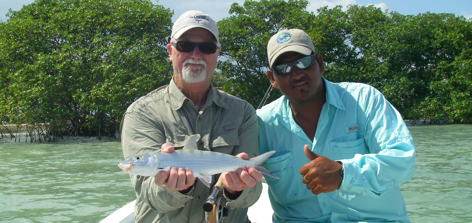 Angler holding a bonefish beside his Belize fishing guide near the mangroves of San Pedro